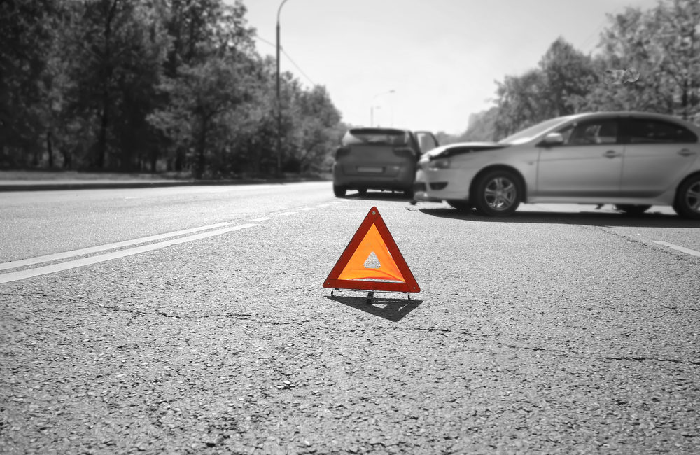 What You Shouldn’t Say At A Car Accident Scene - Car Accident Hazard warning triangle laid out on the road behind two crashed cars, black and white photo with a red accent on a triangle